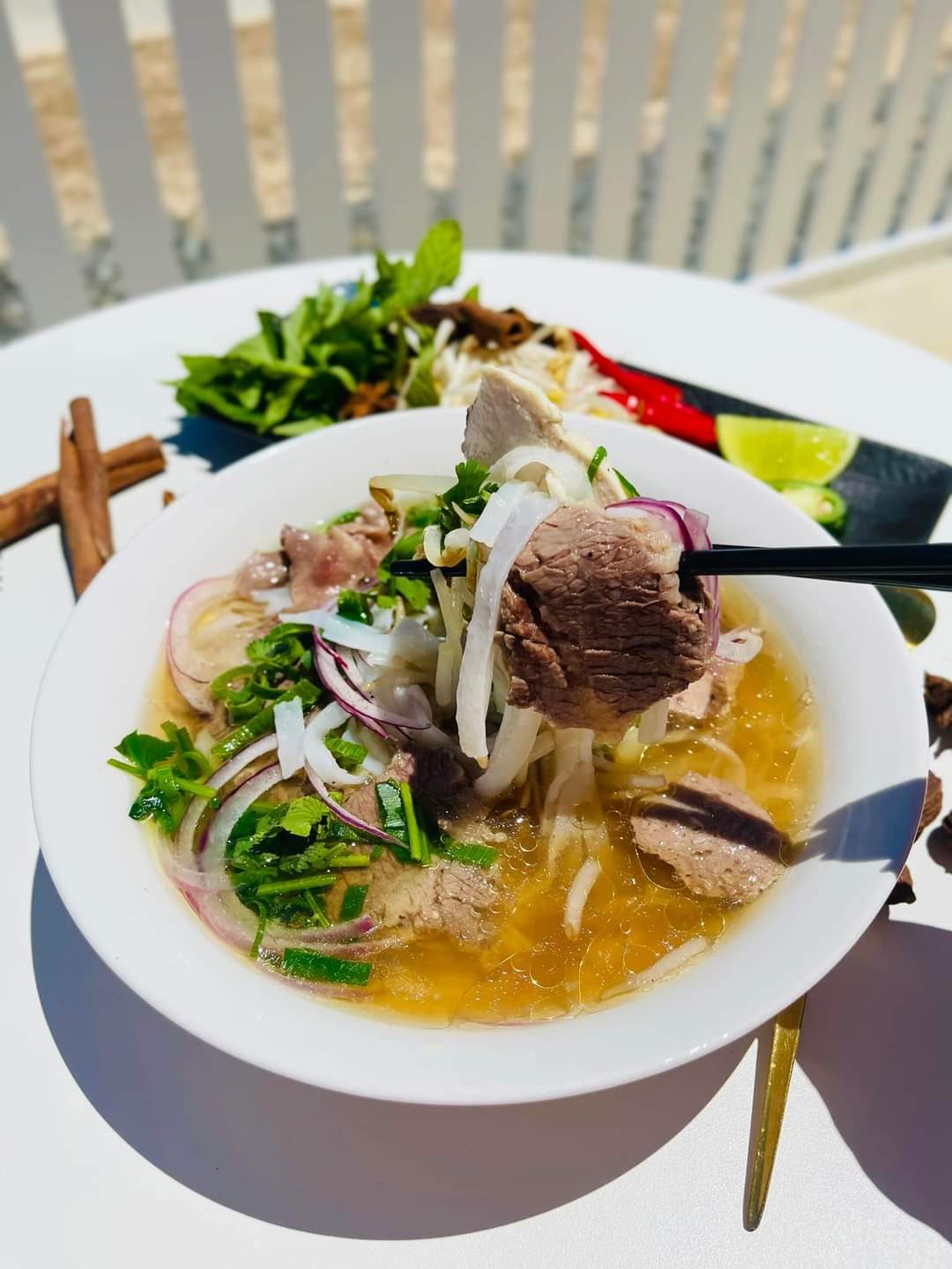 A bowl of beef pho with fresh herbs on the outdoor table